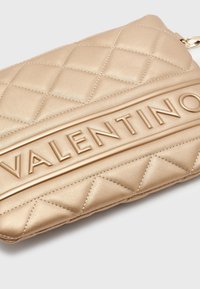 Zlatá prošívaná kožená kabelka s výrazným embossed logem "VALENTINO", která se vyznačuje hladkým povrchem a stylovým diamantovým vzorem.