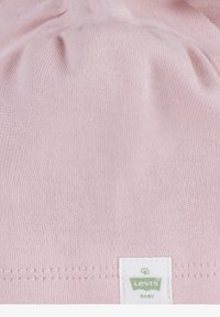 Svijetloružičasti pamukasti odjevni predmet meke teksture s nabranim gornjim dijelom. Ima bijelu etiketu Levi's Baby s zelenim logotipom na dnu.