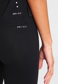 Musta Dri-FIT-leggings, joissa on sileä ja joustava pinta. Huomattavat logokoristeet sijaitsevat vyötärön ja lantion kohdalla.