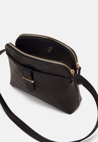 Borsa in pelle nera con stampa a coccodrillo, zip dorata, chiusura magnetica e tracolla slim. Interno spazioso con un compartimento.