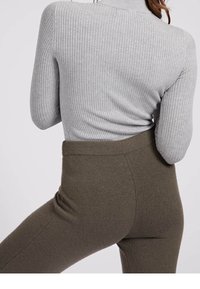 Szary sweter ribbed z wysokim kołnierzem, w połączeniu z oliwkowymi, dopasowanymi spodniami o miękkiej teksturze. Skupienie na detalach tkaniny i kontraście kolorów.