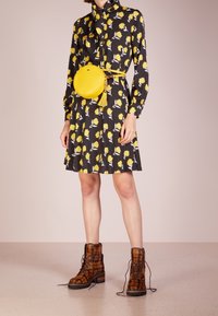 Svart klänning med gult blommönster, gul cirkulärväska med fransar och bruna rutig ankla stövlar. Slät tyg, åtsittande midja, plisserad kjol.