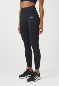 Höga mörkblå leggings med en slät yta och figurnära design, med en logotyp på vänster lår och tonade sid sömmar.