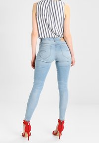 Jeans pitillo de un azul claro con una cintura alta, que cuentan con bolsillos traseros y costuras en contraste, combinados con sandalias de tacón rojo.
