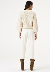 Crème gebreid trui met een textuurpatroon, gecombineerd met witte broek en bruine leren enkelboots met bloemenborduursel.