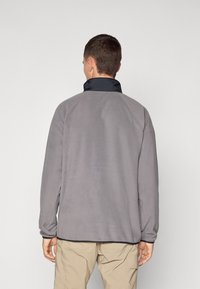 Giacca in pile grigia con colletto alto navy e maniche raglan. Il materiale è morbido e ha una texture liscia. L'orlo presenta un bordo a contrasto.