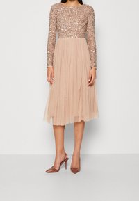 Kortärmad klänning med en paljettprydd överdel och en veckad, semitransparent beige kjol. Matchad med bruna högklackade skor.