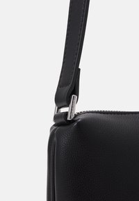 Borsa a mano in pelle nera con una texture granulosa, hardware in argento e una tracolla regolabile. Presenta una forma compatta e rettangolare con chiusura a zip.