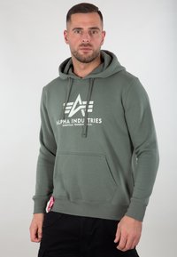Felpa verde con tasca a marsupio, cappuccio con cordino e logo stampato bianco. Polsini e orlo a costine. Tessuto dalla consistenza morbida.