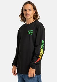 Black long-sleeve shirt with a green logo on the chest and multicolored text down the sleeves in red, yellow, and green. Cotton fabric.