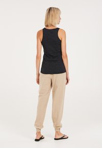 Dunkelgraues Tanktop aus weichem Stoff, kombiniert mit lockeren beigen Hosen. Das Outfit verfügt über elastische Bündchen am Knöchel und schlichte schwarze Sandalen.