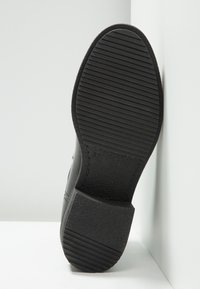 Semelle de chaussure noire avec une surface en caoutchouc texturée et un motif rainuré ; présente un talon bas et un marquage de taille en relief.