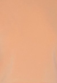 En kvinna i beige träningskläder poserar med armarna korsade, och visar upp en välsittande kortärmad t-shirt och matchande högmidjade leggings.