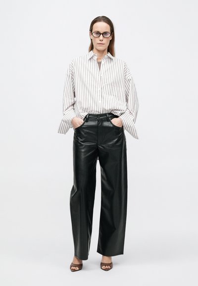 Triibuline pika varrukaga särgiga, millel esiküljel nööbid; kombineeritud kõrge vöökohaga, laiade mustade nahksete pükste ja avatud ninaga pruunide kontsadega sandaalidega.