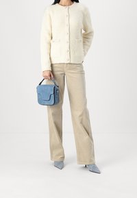 Krämbetongad cardigan med knappar, benfärgade kordbyxor och en liten blå mockaväska med ett handtag. Ljusblå spetsiga klackskor.