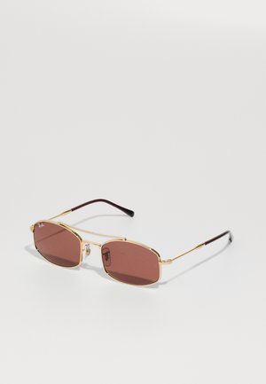 Kultaiset Ray-Ban aurinkolasit, joissa on suorakulmaiset ruskeat linssit ja ohuet sankat, lepo valkoisella pinnalla.