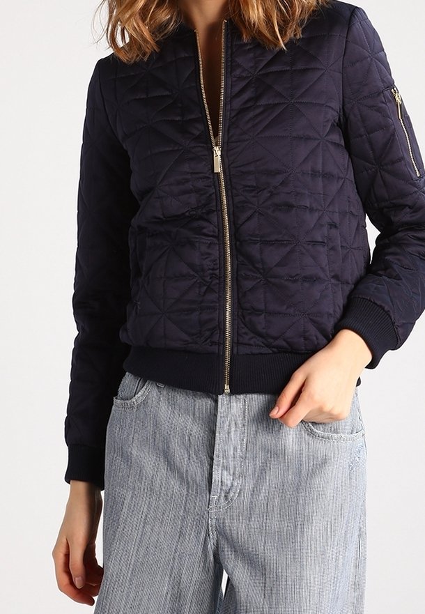 Chaqueta bomber acolchada en color navy con cremallera dorada, puños acanalados y bolsillos laterales. Textura de tela suave con un diseño ajustado.