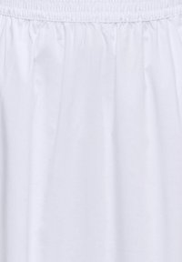 Tissu blanc avec ceinture élastique, texture lisse et plis légèrement froncés.