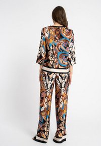 Sukienka z jedwabiu składająca się z luźnego topu i spodni o szerokich nogawkach, zdobiona kolorowymi abstrakcyjnymi wzorami w odcieniach brązu, czerni, niebieskiego i beżu.