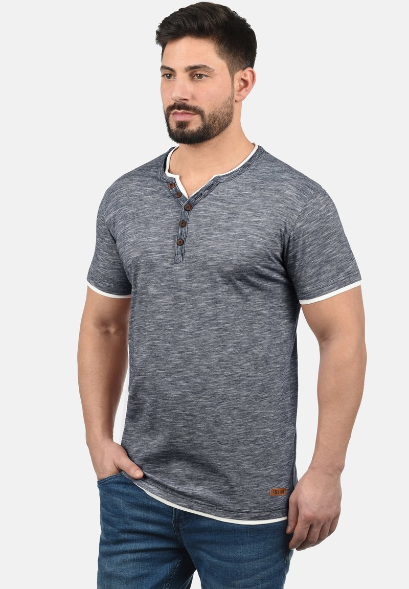 Marineblå kortermet henley-skjorte laget av teksturert stoff, med hvit kanting og tre brune knapper ved halsen.