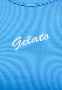 Κοντινό πλάνο σε γαλάζιο ριμπ ύφασμα με τη λέξη "Gelato" κεντημένη με λευκά γράμματα σε καλλιγραφικό στυλ.