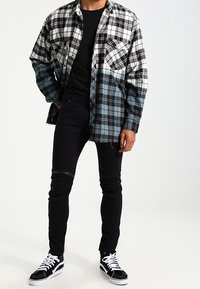 Černobílá kostičkovaná flanelová košile se světle modrými detaily, spárovaná s černými skinny džíny a černobílými teniskami.