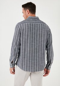 Camisa de hombre de manga larga en gris con rayas verticales blancas. Presenta un cuello abotonado y detalles en los puños. Tejido texturizado con un ajuste relajado.