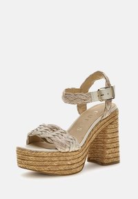Woven beige platform sandal with a chunky, braided heel, ankle strap, and smooth footbed. Features a glossy white buckle and texture contrast.