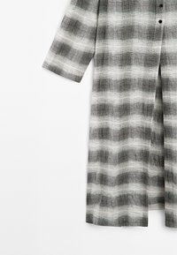 Zwart-witte gestreepte lange shirt, met een knoopsluiting aan de voorkant, brede mouwen en een zachte, gestructureerde stof met een geruit patroon.