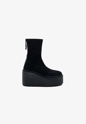 Bottines en suede noir avec un haut plateau et une semelle épaisse à stries. Comprend une fermeture zippée sur le côté et une finition lisse et texturée.