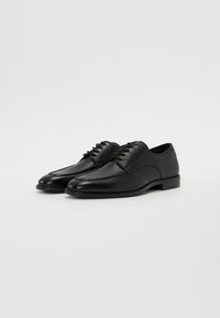 Scarpe da uomo in pelle nera con texture liscia, forma a punta, design stringato e tacco basso e arrotondato.