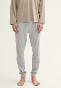 Lichtbruine long-sleeve shirt gedragen met grijs gestreepte pyjamabroek, met een ontspannen pasvorm en omgeslagen pijpen, blote voeten.