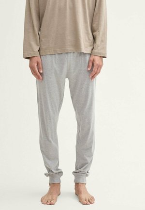 Chemise à manches longues marron claire associée à un pantalon de pyjama gris rayé, avec une coupe décontractée et des ourlets côtelés, portée pieds nus.
