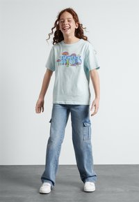 Lyseblå bomull T-skjorte med fargerik grafisk design, sammen med løst sittende lyse denim cargo-bukser med sidelommer.