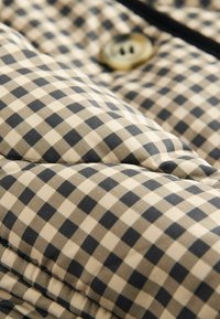 Tissu matelassé à motif carreaux beige et noir, mettant en avant un bouton rond doré et une surface texturée.