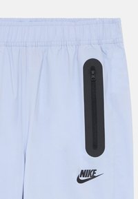 Gaiši zili Nike šorti ar elastīgu jostu, melna vertikāla rāvējslēdzēja kabata labajā pusē un melns Nike logo zem kabatas.
