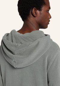 Grå hoodie med en avslappnad passform, med dragsko i huvan och en slät textur. Synlig sömnad längs sömmarna ger detalj.