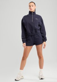 Navy blue cropped sweatshirt with high collar ja hõbedase tõmblukuga, koos vastava lühikestega. Sile kangas ja mugav lõige.