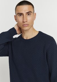 Pulover tricotat de culoare bleumarin, cu un model texturat în formă de fagure, guler rotund și manșete cu nervuri, având un design ajustat.