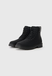 Botas de tobillo negras con cordones, hechas de material suave, que cuentan con un cuello acolchado, punta redondeada y suela de goma resistente con patrones de tracción.
