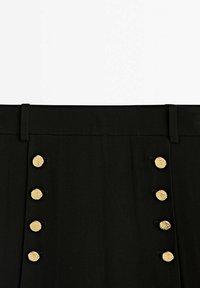 Panneau en tissu noir avec deux rangées de quatre boutons dorés texturés chacun, disposés verticalement près du bord supérieur avec des passants de ceinture au-dessus.