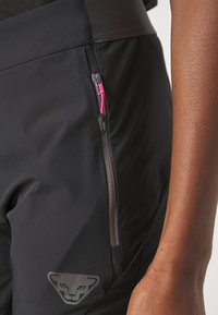 Sorte treningbukser med en sidelomme med glidelås og rosa detaljer. Glatt, elastisk stoff med et subtilt logodesign nær kanten.
