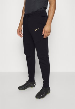 Schwarze sportliche Jogginghosen mit schmaler Passform, ausgestattet mit einem goldenen Nike-Logo, Kordelzugbund und seitlichen Taschen. Getragen mit schwarzen Sportschuhen.