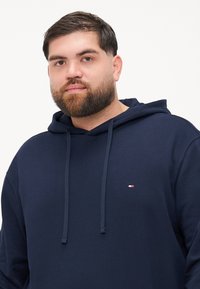 Felpa blu navy realizzata in tessuto morbido, con tasca a marsupio frontale e cappuccio con cordino, caratterizzata da un piccolo logo sul petto.