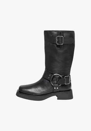 Stivale nero in pelle alto fino al ginocchio con gambale largo, dettagli in fibbia argentata, cinturino spesso con accessori circolari e suola robusta a piattaforma.