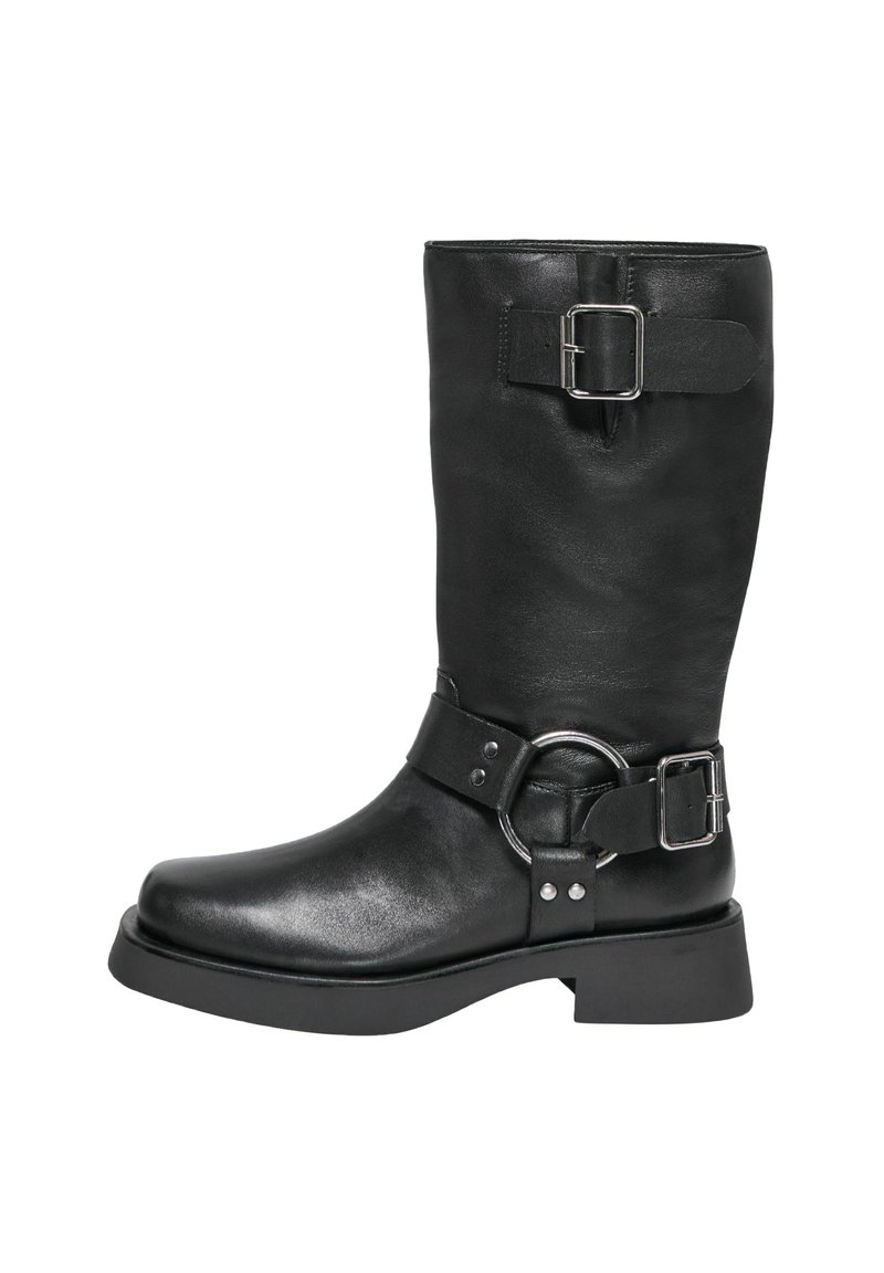 Stivale nero in pelle alto fino al ginocchio con gambale largo, dettagli in fibbia argentata, cinturino spesso con accessori circolari e suola robusta a piattaforma.