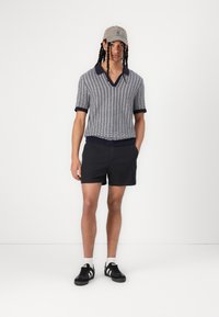 Polo tricoté à manches courtes en bleu marine et blanc avec un col en V et un col contrastant, associé à un short noir et des baskets noires avec des rayures blanches.
