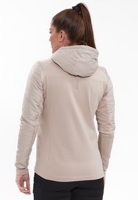 Beige jakke med hætte, der har et tætsiddende design, blødt materiale og strukturerede ærmer. Behagelige sømdetaljer fremhæver det overordnede udseende.