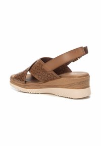 Sandalia de cuero perforado marrón con tacón de cuña, que presenta un diseño de tiras cruzadas y una suela de goma beige con fondo texturizado.