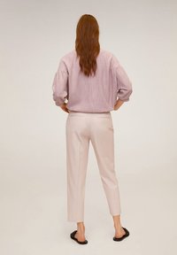 Lichtroze oversized overhemd met gestructureerde stof en pofmouwen, gecombineerd met taps toelopende crèmekleurige broek en zwarte slides.